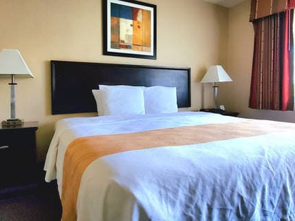 A neatly made hotel bed with white linens, a beige blanket runner, dark headboard, two nightstands with lamps, and a framed picture above.