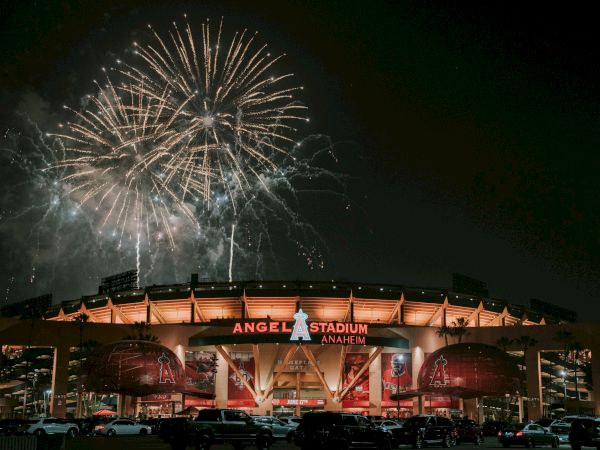 Fireworks explode above Angels Stadium in Anaheim at night, lighting up the sky as the stadium facade glows warmly below.