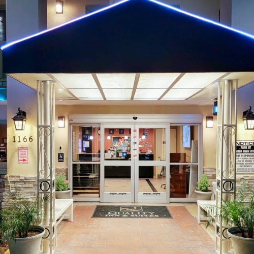 A bright, welcoming storefront or small venue with a blue canopy, glass doors, and warm lights, inviting guests to enter, cozy and inviting.