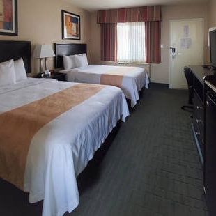 A hotel room with two queen beds, a desk, a television, and a window with curtains; neutral decor and wall art.