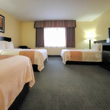 A hotel room with three beds, a window with curtains, a desk and TV, neutral lighting, and beige walls. End the sentence.