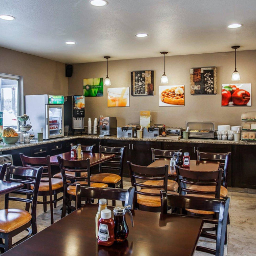 A cozy caf&eacute; with wooden tables and chairs, a self-serve counter, condiments on tables, and bright overhead lights in a warm setting.